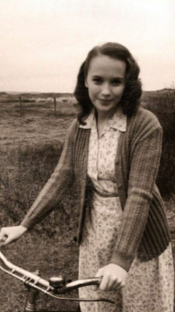 Vintage family photo: a smiling girl with her bicycle in an open field