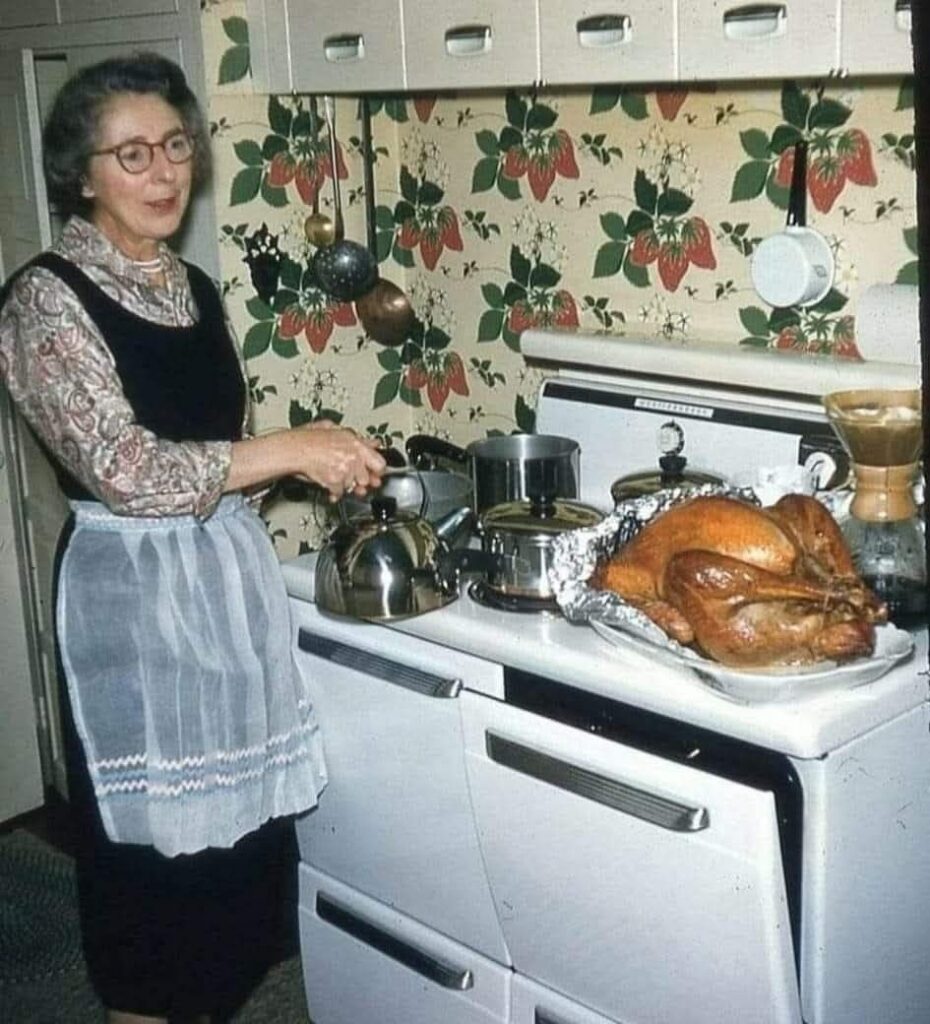 Vintage family photo: a grandmother cooking at the stove in a strawberry-papered kitchen