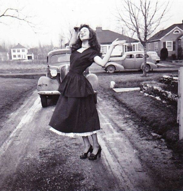 Vintage photo: a woman posing on a country lane beside vintage cars