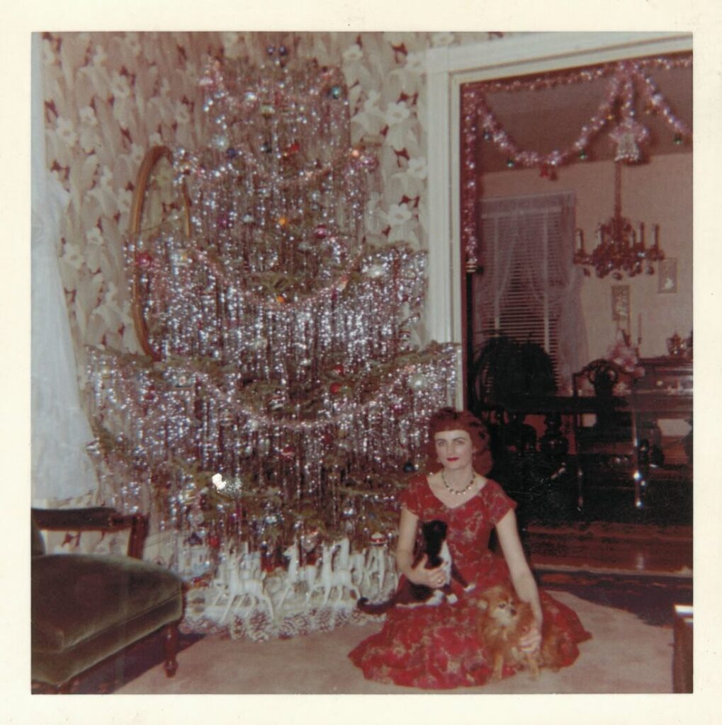 Vintage photo: a woman beside a large tinsel Christmas tree with a cat and a dog